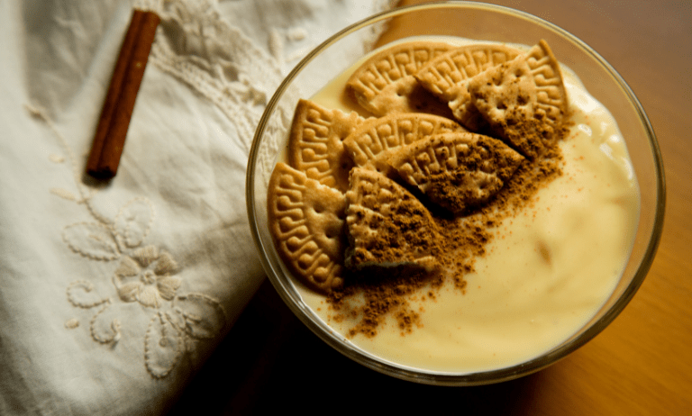 Una exquisita copa de natillas con galletas María, adornada con canela espolvoreada. Un deleite visual que invita a saborear la tradición y la indulgencia culinaria en cada cucharada.